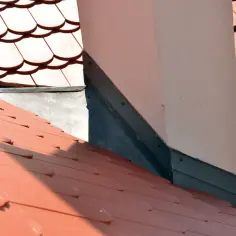 Szczelne okucie komina blachą, chroniące dach przed wilgocią. Czerwona dachówka tworzy tło dla tej ważnej instalacji.