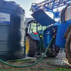 Duży zbiornik na deszczówkę Kingspan AquaBank podłączony wężem do traktora. Zastanawiasz się, czy zbiornik na deszczówkę wymaga zgłoszenia?