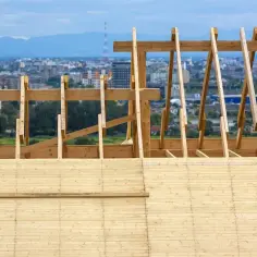 Drewniana konstrukcja dachu, widok na miasto w tle. Ażurowe deskowanie tworzy szkielet przyszłego pokrycia.