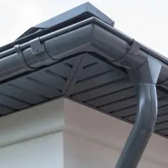 Szary system rynnowy z rurą elastyczną do rynny, zamontowany na rogu dachu.