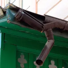 Uszkodzone uszczelnienie rynny plastikowej wymaga naprawy. Brązowa rynna odprowadza wodę z dachu.