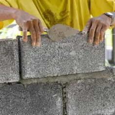 Murarz układa bloczek betonowy, dbając o jego wymiary i równość.