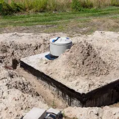 Betonowe szambo w wykopie, z widoczną izolacją i rurą odpływową.