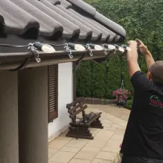 Mężczyzna mocuje lampki choinkowe do podbitki, używając klipsów.