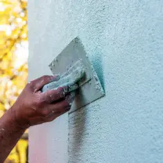 Dłoń z kielnią tworzy na ścianie charakterystyczną, ziarnistą strukturę elewacyjną.