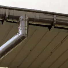 Brązowa rynna z odpływem, widoczny jest jej spadek na rynnie, który zapewnia prawidłowe odprowadzanie wody deszczowej.