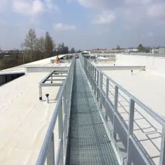 Szeroki dach pokryty białą membraną TPO, z metalową kładką serwisową biegnącą wzdłuż.