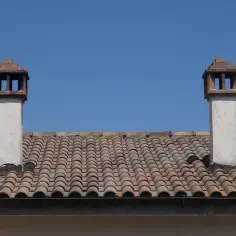 Dwa kominy na tle błękitnego nieba, osadzone na ceramicznym opierzeniu dachu.