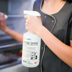 Osoba w fartuchu czyści lodówkę, trzymając w dłoni butelkę z preparatem FRIDGE SHINE. To prosty sposób, jak wyczyścić uszczelki w lodówce.