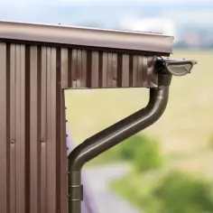 Nowy, brązowy system rynnowy zamontowany na ścianie starego domu. Wymiana rynien poprawia estetykę i funkcjonalność.