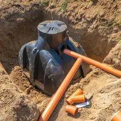Instalacja szamba w wykopie, przygotowanie do zasypania. Widać rury drenażowe i akcesoria. Kluczowe jest, jak głęboko zakopać rury drenażowe.