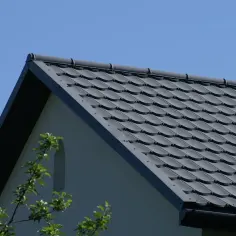 Szary dach dwuspadowy z dachówki ceramicznej na tle błękitnego nieba.