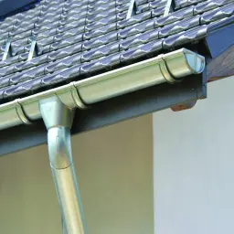 Przegląd dachu: nowe, metalowe rynny i rury spustowe zamontowane pod ciemnymi dachówkami.