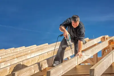 Budowniczy wierci otwór w drewnianej belce, przygotowując wypuszczenie dachu na łatach.